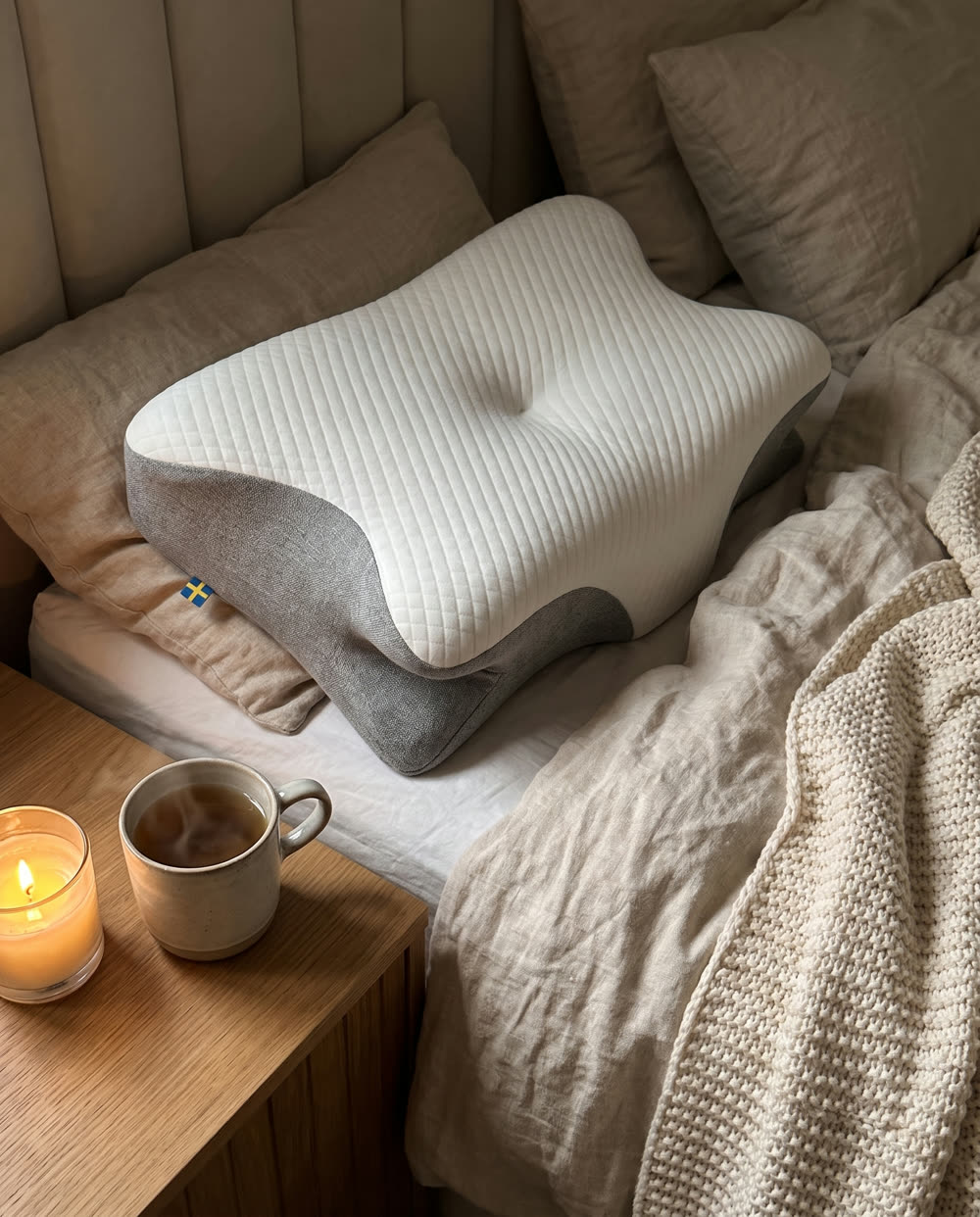 SleepEase-kussen op bed met gebreide plaid en thee op het nachtkastje